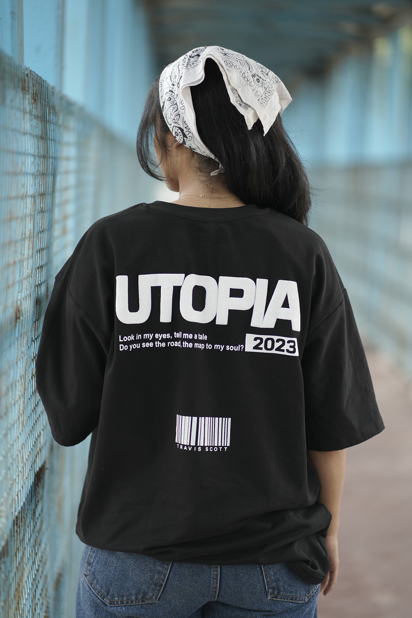 Person wearing a BLACK shirt with 'UTOPIA' printed on it, walking on a road.
